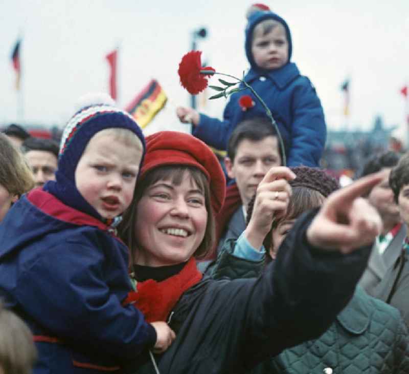 Freudestrahlend zeigt eine Mutter ihrem Kind mit ausgestrecktem Arm die Ehrentribüne zur traditionellen Demonstration am 1. Mai 197