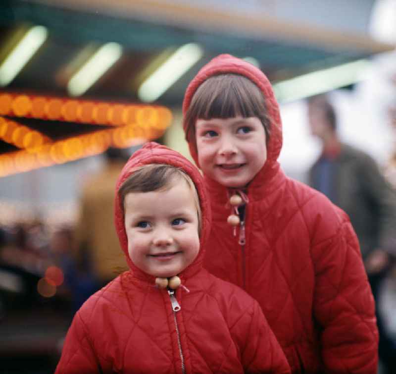 Nicht nur die roten Jacken der zwei Mädchen leuchten auf dem Weihnachtsmarkt am Berliner Alexanderplatz, auch die Gesichter strahlen vor Freude über den großen Rummel.