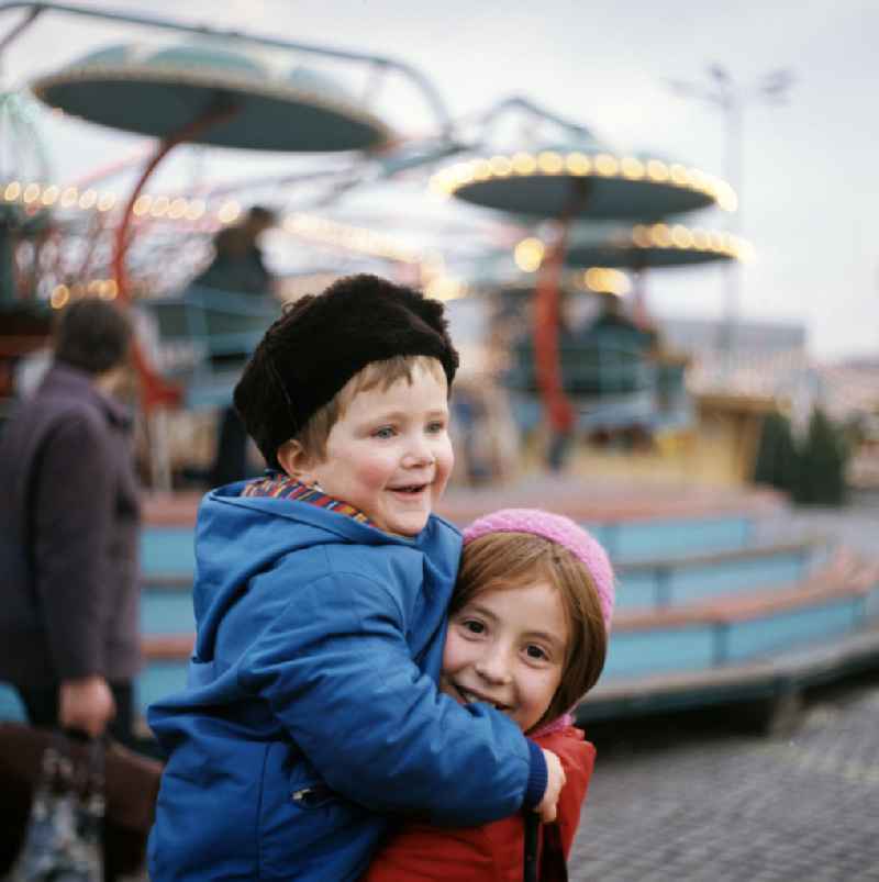 Zwei Kinder amüsieren sich auf dem Weihnachtsmarkt am Berliner Alexanderplatz - hier hebt ein Mädchen lachend ihren kleinen Bruder auf den Arm.