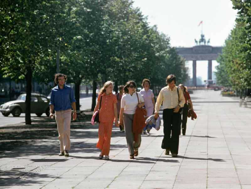 Touristen flanieren auf der Prachtstraße Unter den Linden in Berlins Mitte und genießen die ersten warmen Sonnenstrahlen des Jahres, im Hintergrund Blick auf das Brandenburger Tor.