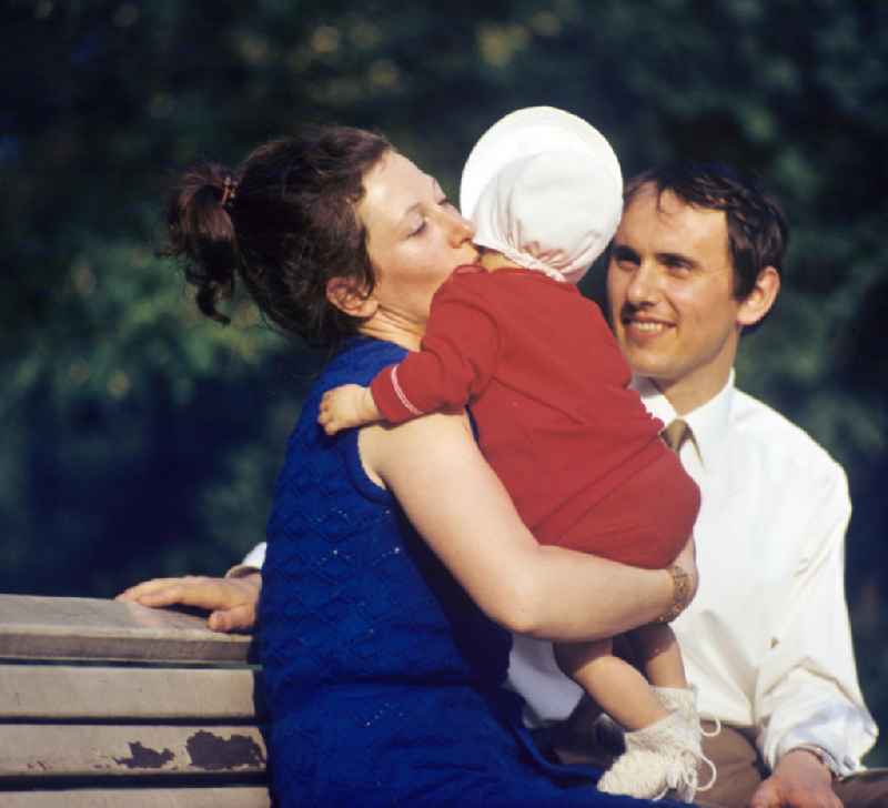 Ein Paar mit Baby genießt im Volkspark Friedrichshain in Berlin sein junges Familienglück.