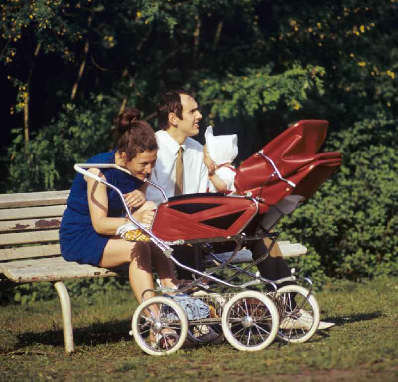 Ein Paar mit Baby im Kinderwagen genießt im Volkspark Friedrichshain in Berlin sein junges Familienglück.