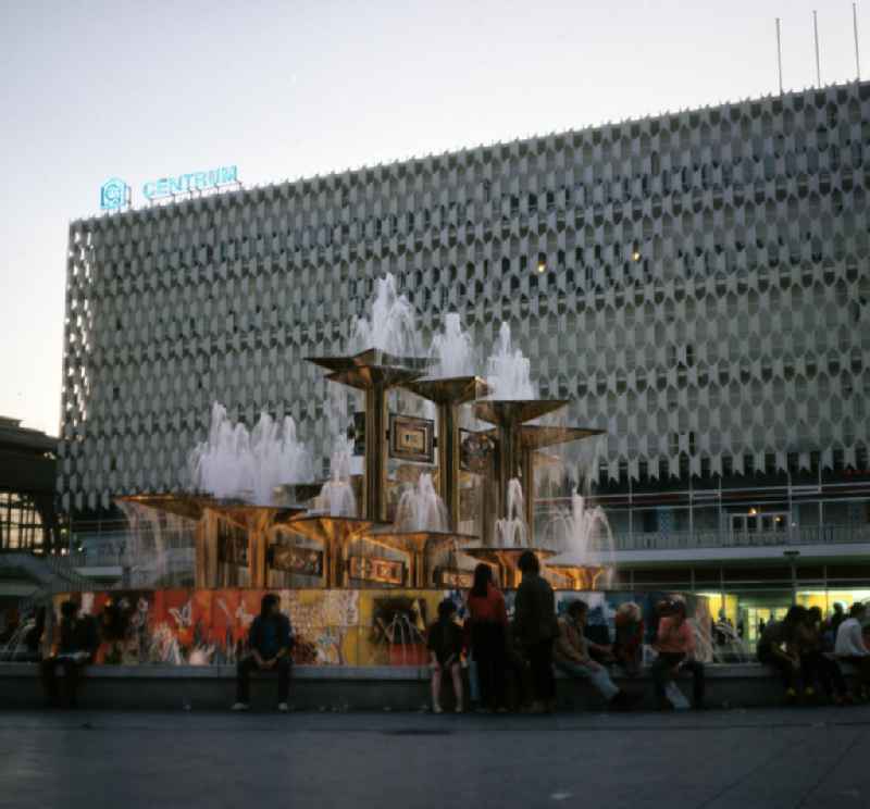 Touristen und Einheimische sitzen am Brunnen der Völkerfreundschaft, umgangssprachlich Nuttenbrosche, auf dem Berliner Alexanderplatz. Der 197
