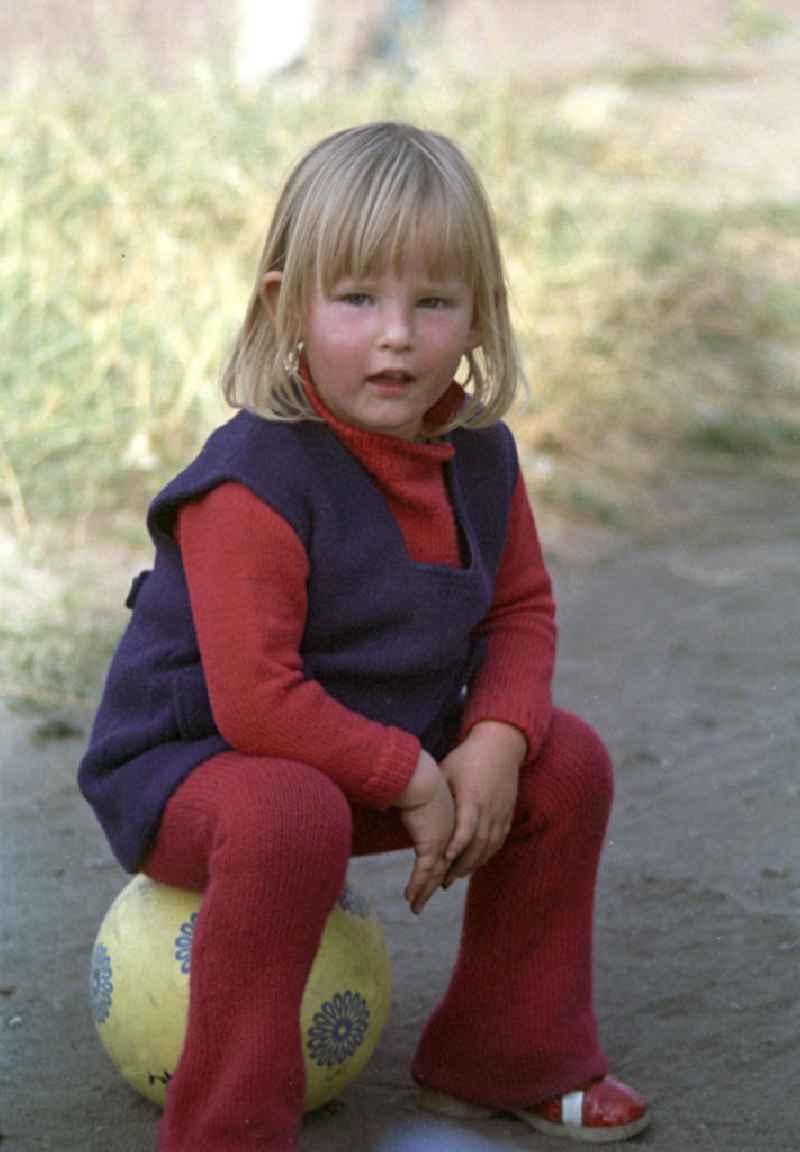Ein kleines Mädchen sitzt im für die Zeit typischen Strickanzug auf einem Ball.