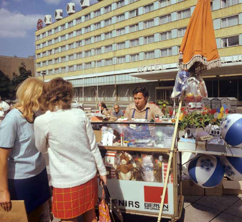 Zu den Weltfestsielen im Sommer 1973 in Berlin können Touristen an einem Souvenirstand vor dem Interhotel 'Unter den Linden' in Berlin-Mitte können Touristen kleine und große Andenken an ihren Aufenthalt erwerben - vom Farbfilm über Miniaturfernsehtürme und den Berliner Bären in verschiedenen Ausführungen bis hin zum Wasserball mit dem Weltfestspiele-Logo fehlt es hier an nichts. Das Mitte der 60er Jahre errichtete Hotel an der Friedrichstraße / Ecke Unter den Linden war eines der ersten Neubauten der Interhotel-Kette der DDR. Das Gebäude wurde 20