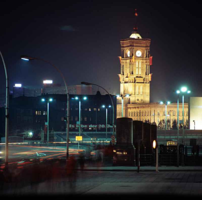 Nachtaufnahme: Blick auf das Rote Rathaus vom Marx-Engels-Platz (heute Schlossplatz) in Berlin-Mitte zum 20. Jahrestag der DDR. Auf den Granitsockeln mit den hohen Marmor-Postamenten fehlen noch die historischen Brückenfiguren, diese wurden erst 1983 wieder aufgestellt. Das Gebäude auf dem heutigen Marx-Engels-Forum (l) wurde in 7