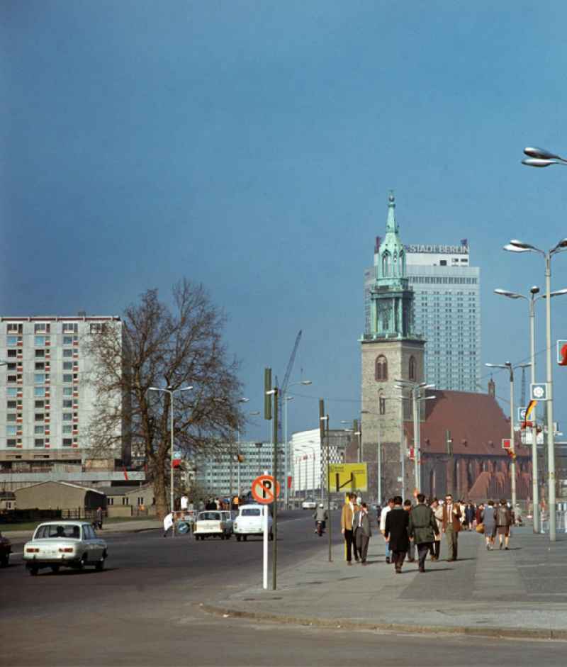 Passanten laufen entlang der Karl-Liebknecht-Straße in Berlin. Im Hintergrund die Marienkirche, umgeben von den gerade neu errichteten Neubauten sozialistischer Architektur. Links im Bild fehlt noch das Palasthotel. Dieser Hotelkomplex an der Spree wurde erst in der Zeit zwischen 1976 bis 1979 errichtet.