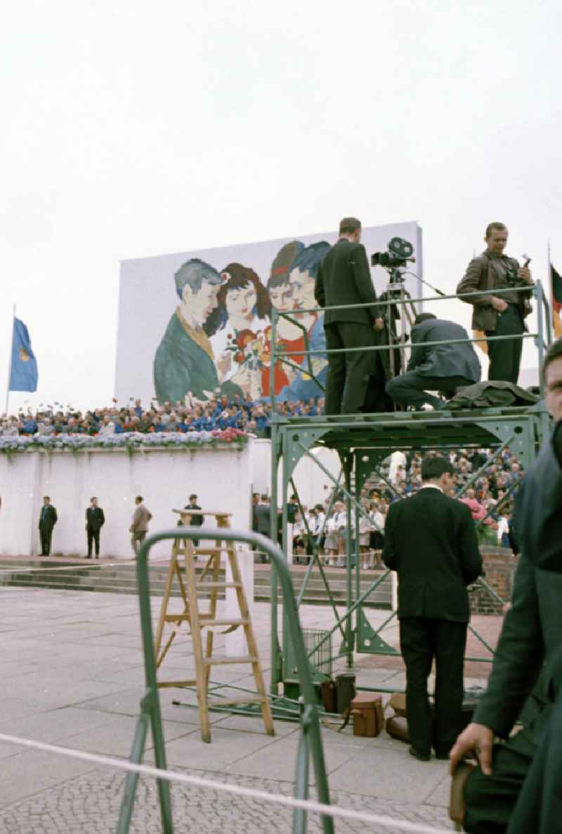 Zu Pfingsten 1964, vom 16.-18. Mai, findet in Berlin das letzte 'Deutschlandtreffen der Jugend für Frieden und Völkerfreundschaft' statt, Fotografen und Kameraleute halten den Aufmarsch vor der Ehrentribüne auf dem Marx-Engels-Platz (heute Schloßplatz) im Bild fest. Ziel der ersten Veranstaltung im Mai 1950 war, die kommunistische Jugend in Ost und West mobil zu machen und der damals in der BRD noch zugelassenen FDJ neue Anhänger zuzuführen. 1951 wurde das Verbot gegen die FDJ in der BRD ausgesprochen. Nach 1964 entsprach eine gesamtdeutsche kommunistische Politik nicht mehr den Zielen der DDR-Regierung. In den 70er und 8