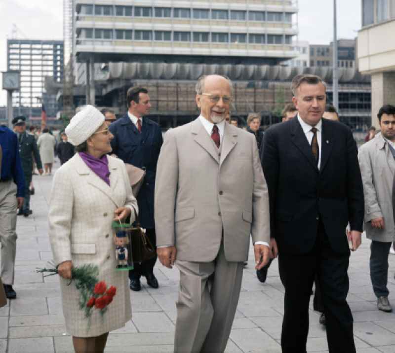 Der Erste Sekretär der SED und Vorsitzende des Staatsrates der DDR, Walter Ulbricht, geht mit seiner Ehefrau Lotte auf der Karl-Marx-Allee nahe Alexanderplatz entlang. Im Hintergrund das Haus des Reisens, dahinter der Rohbau des Berliner Verlages.