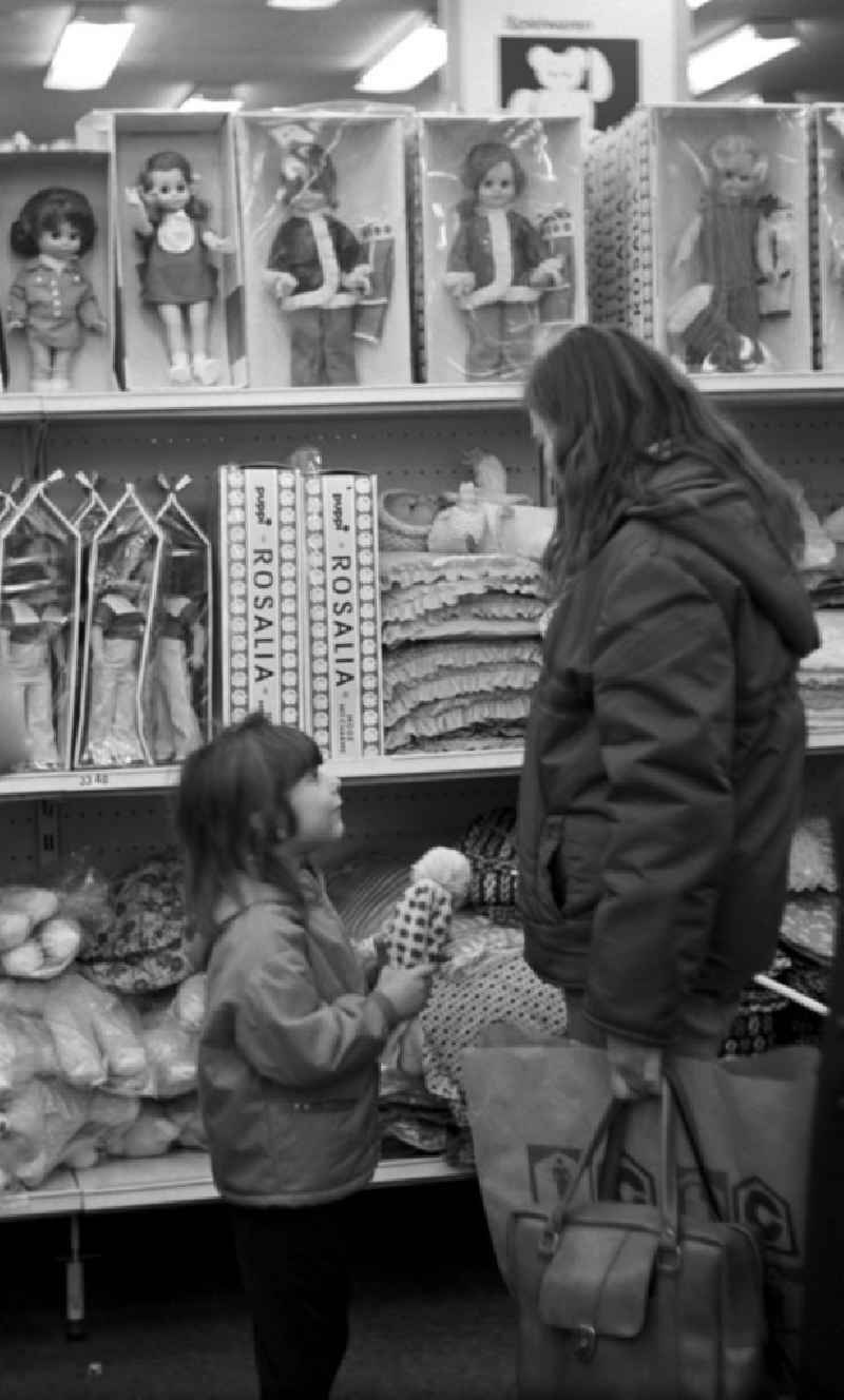 Bittend schaut ein Mädchen die Mutter in der Spielwarenabteilung im Centrum Warenhaus am Alex in Berlin vor einem Regal mit Puppen an.
