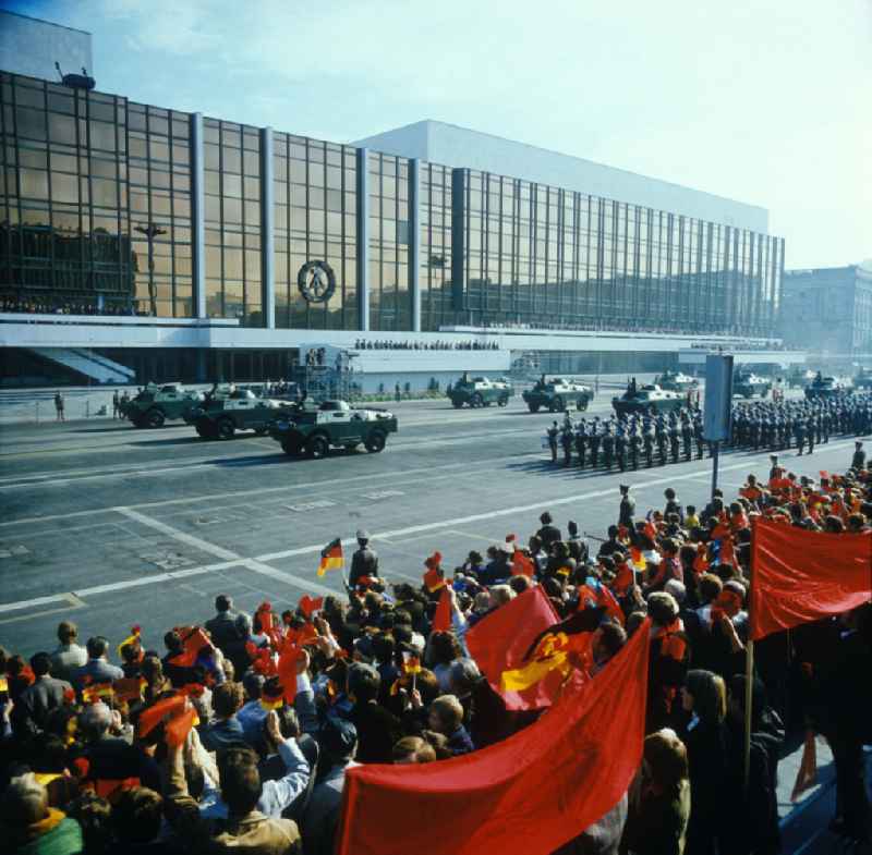 Parade der NVA auf dem Schloßplatz zum 28. Jahrestag der DDR. Soldaten und Schützenfahrzeuge vor dem PdR. Zuschauer mit Winkelementen im Vordergrund. Im Hintergrund der Palast der Republik mit Tribünen. Symbol / Emblem der DDR an der GlasFassade des PdR.