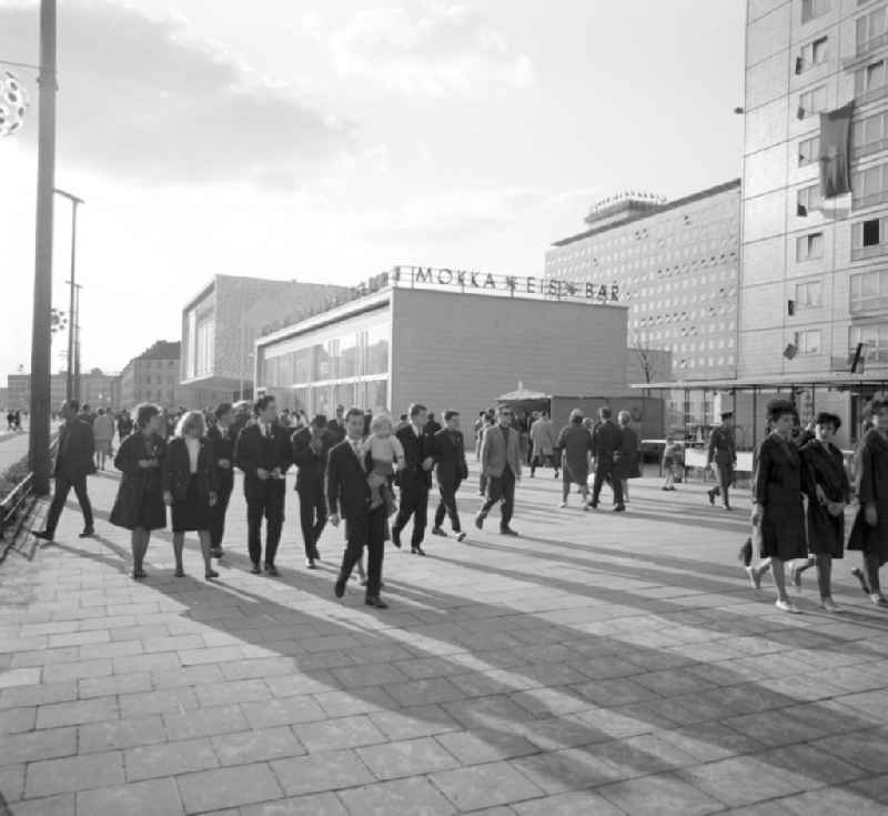 Zu Pfingsten 1964, vom 16.-18. Mai, findet in Berlin das letzte 'Deutschlandtreffen der Jugend für Frieden und Völkerfreundschaft' statt - hier herrscht vor dem Kino International und der Mokka-Eis-Bar reges Treiben auf der Karl-Marx-Allee, im Hintergrund das Hotel Berolina. Ziel der ersten Veranstaltung im Mai 1950 war, die kommunistische Jugend in Ost und West mobil zu machen und der damals in der BRD noch zugelassenen FDJ neue Anhänger zuzuführen. 1951 wurde das Verbot gegen die FDJ in der BRD ausgesprochen. Nach 1964 entsprach eine gesamtdeutsche kommunistische Politik nicht mehr den Zielen der DDR-Regierung. In den 70er und 8