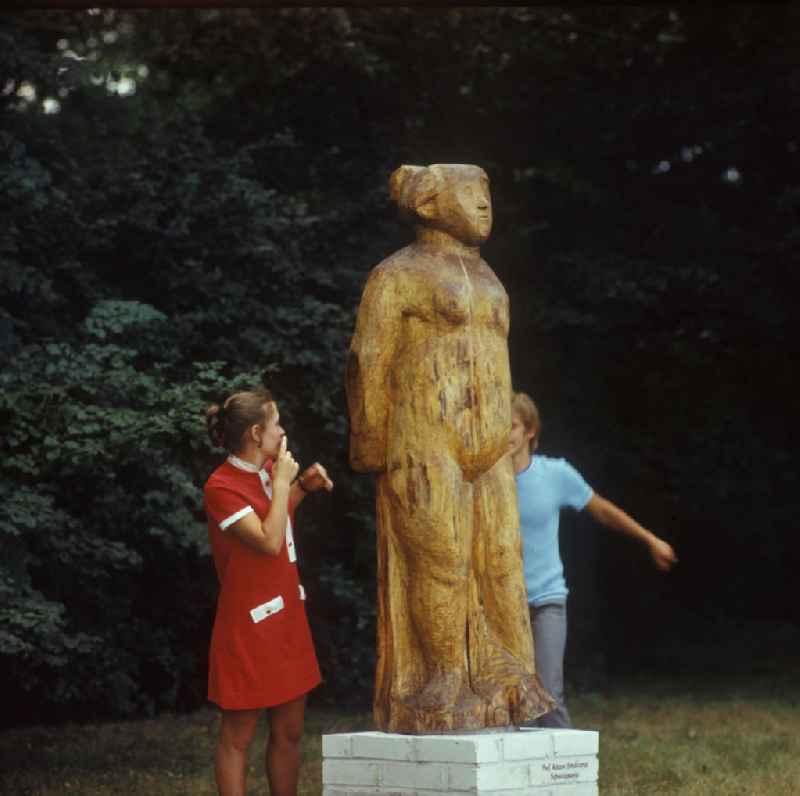 Junges Pärchen in einem Berliner Park neben einer Holzskulptur 'Schweigsame' des Bildhauers Prof. Adam Smolana (1921-1987). Jung couple in a park beside a wood sculpture of the carver Adam Smolana.