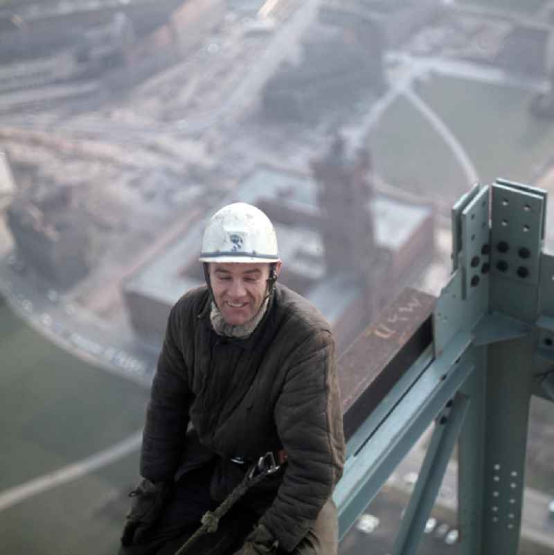 Ein Bauarbeiter in luftiger Höhe auf dem Fernsehturm in Berlin. Im Hintergrund ist das Rote Rathaus zu erkennen.