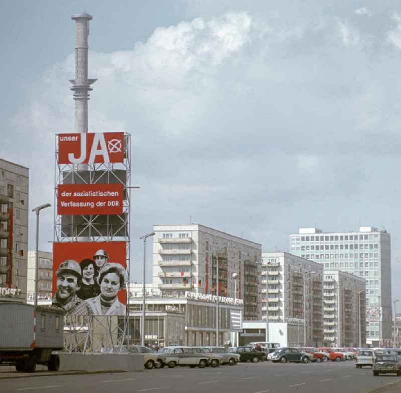 Ein Propagandaschild mit der Losung 'Unser JA der sozialistischen Verfassung der DDR' steht auf der Karl-Marx-Allee in Berlin. Hinter dem Schild das Café Moskau und der im Bau befindliche Fernsehturm.