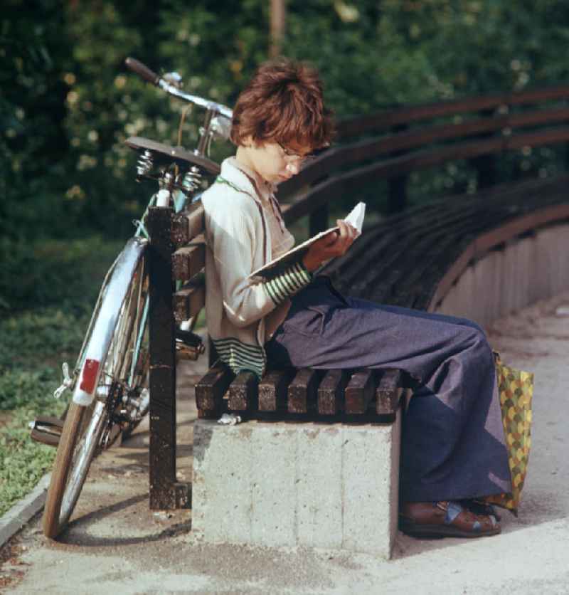 Ein Junge liest auf einer Bank in einem Park in Berlin ein Buch.