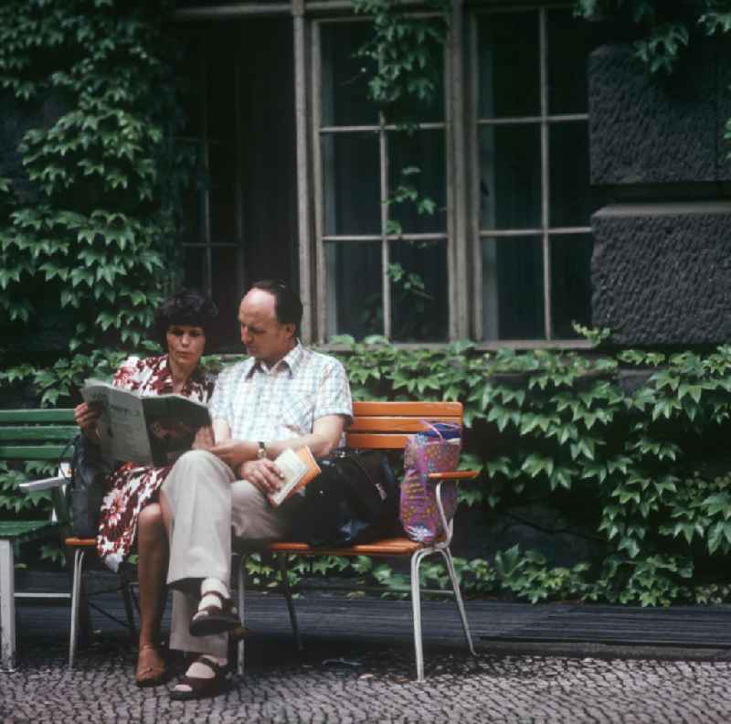 Ein Paar sitzt im Hof der Deutschen Staatsbibliothek Unter den Linden in Berlin-Mitte und liest gemeinsam eine Zeitschrift.