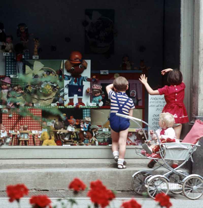 Kinder schauen neugierig durch das Schaufenster eines Spielzeugladens in Berlin, in dem vor allem Puppen, Teddys und ein Puppentheater ausgestellt sind.