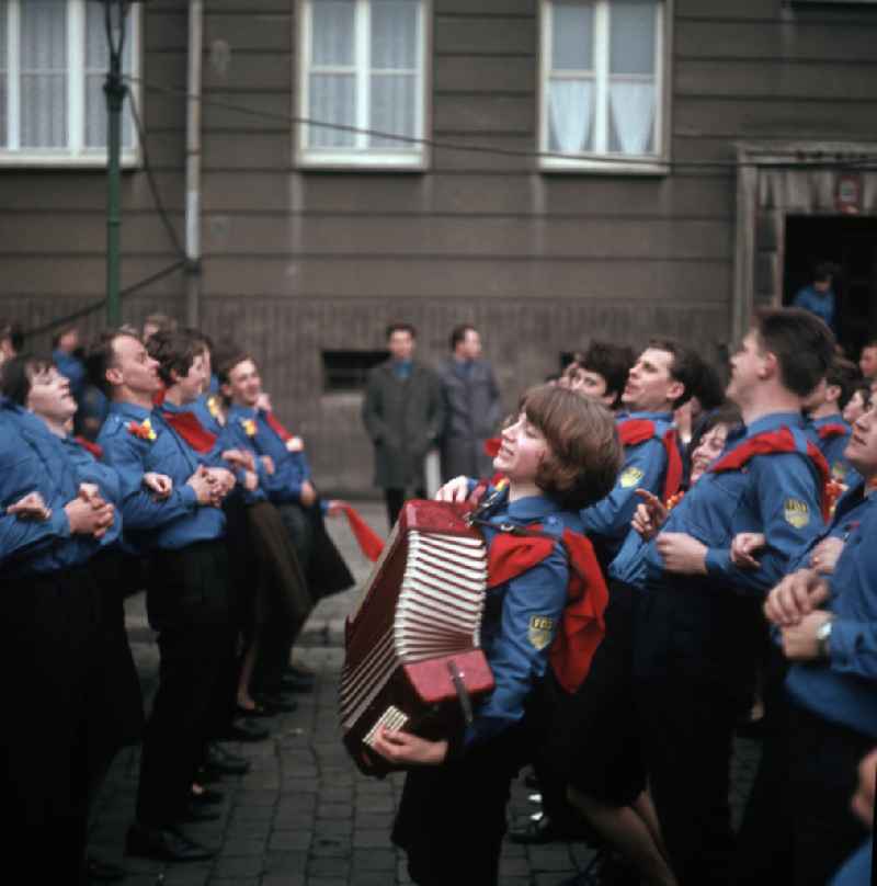 Auf einer Jugenddemonstration singen und tanzen FDJler in Uniform zur Musik eines Akkordeons in Berlin.