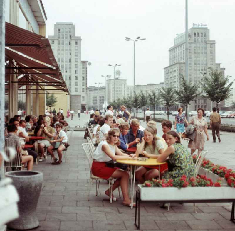 Moderne Neubauten sollen Ost-Berlin als Hauptstadt der DDR das Antlitz einer sozialistischen Großstadt verleihen - hier Familien beim Eisessen in der beliebten Mokka-Milch-Eisbar an der Karl-Marx-Allee. Im Hintergrund die Hochhäuser am Strausberger Platz. Der bestehende Wohnungsmangel entwickelte sich in der DDR seit den 6