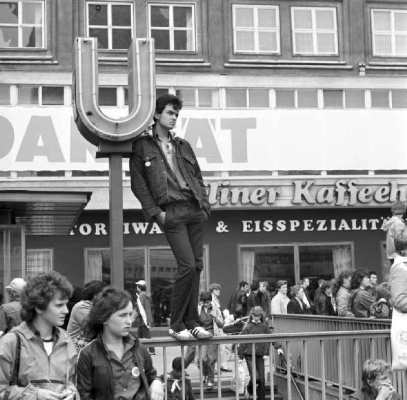 Zum Pfingsttreffen der FDJ in Berlin beobachtet ein Jugendlicher vom Geländer des U-Bahn-Eingangs das Treiben auf dem Alexanderplatz. Bei den alle fünf Jahre stattfindenden Pfingsttreffen kamen Zehntausende delegierte Mitglieder der FDJ aus der ganzen DDR zusammen.