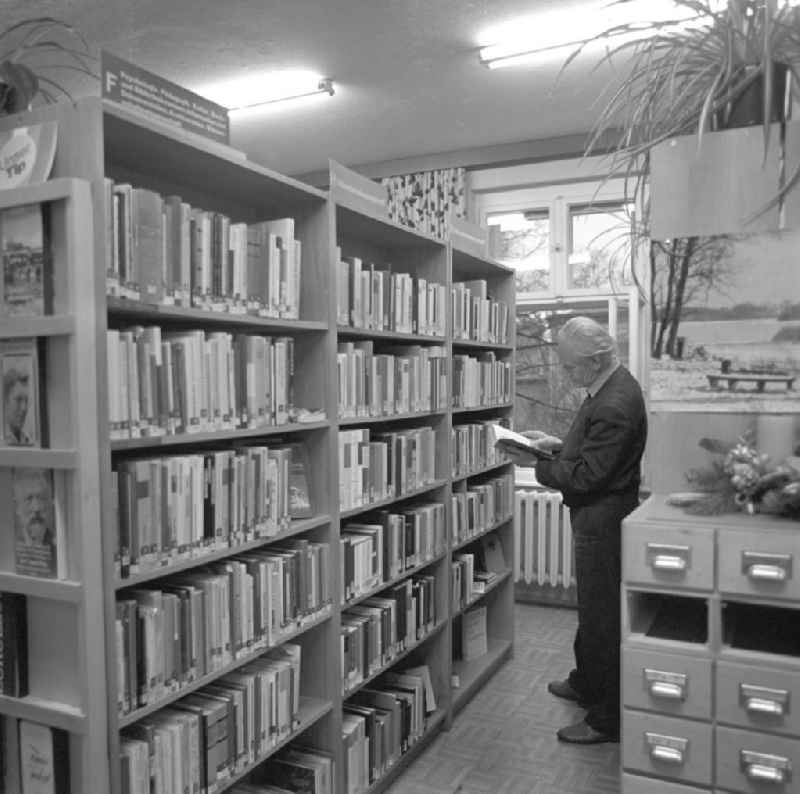 Veranstaltung mit dem Komponisten Kurt Schwaen in einer Bibliothek in Berlin-Mahlsdorf - Kurt Schwaen steht in einer Regalreihe und blättert in einem Buch.