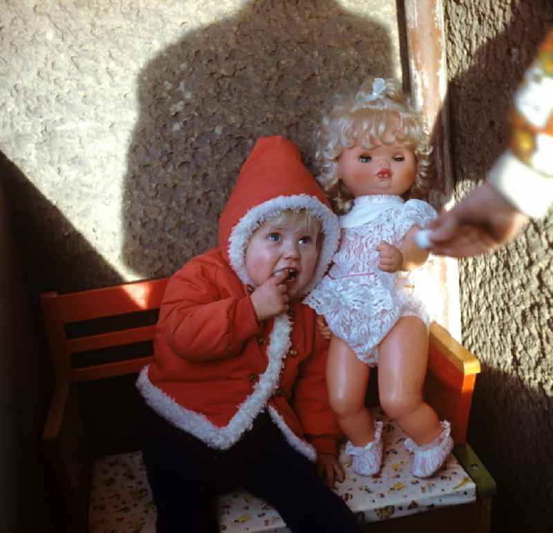 Kleines Kind in ' Weihnachtsmann-Jacke ' mit Puppe, aufgenommen in den 197