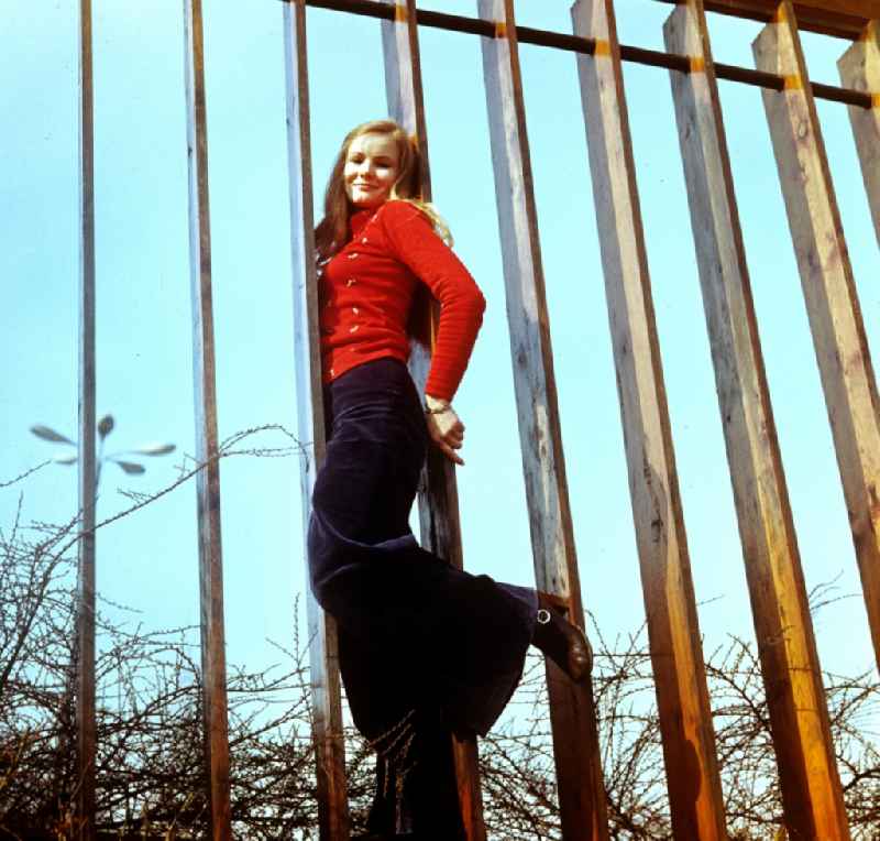 A young woman in shock trousers posing on a metal fence