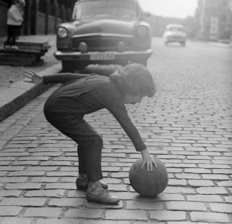 A child plays with a ball on the street in Berlin. In the background is a parked Auo type Volga