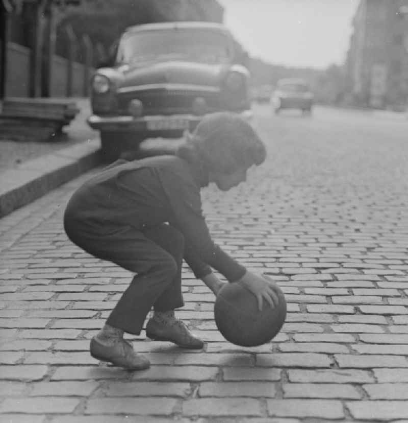 A child plays with a ball on the street in Berlin. In the background is a parked Auo type Volga