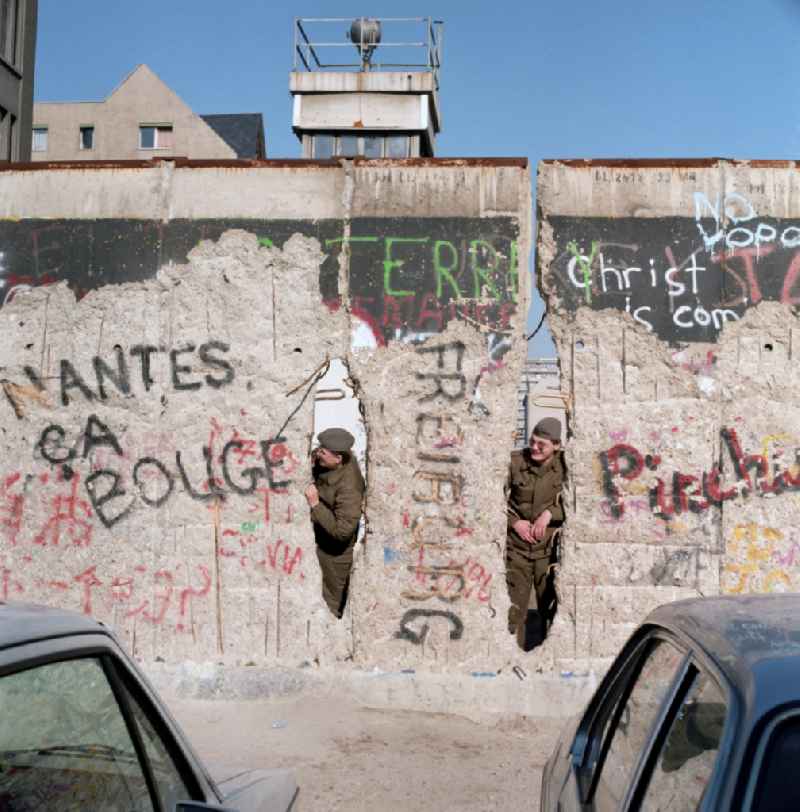 Two soldiers of the Border Troops of the GDR look through a hole in the Berlin Wall in Berlin