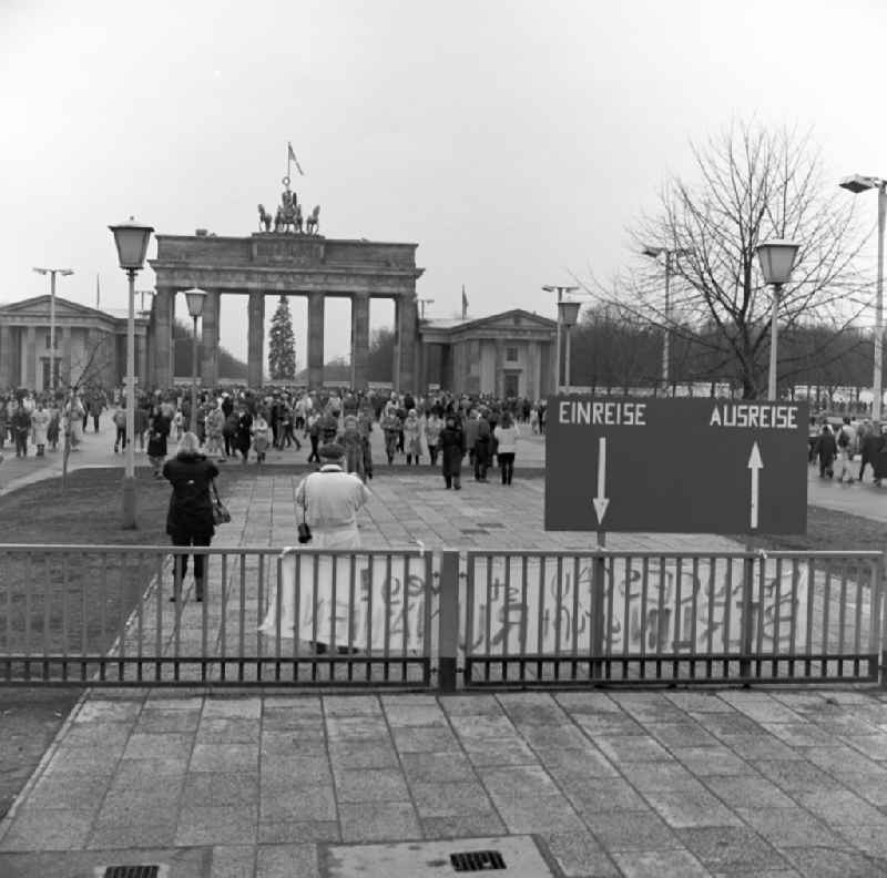 Tourists and Berlin citizens walk shortly before the fall of the Wall at the Brandenburg Gate in Berlin. In the background is still closed Berlin Wall. In the foreground a sign that read entry / departure