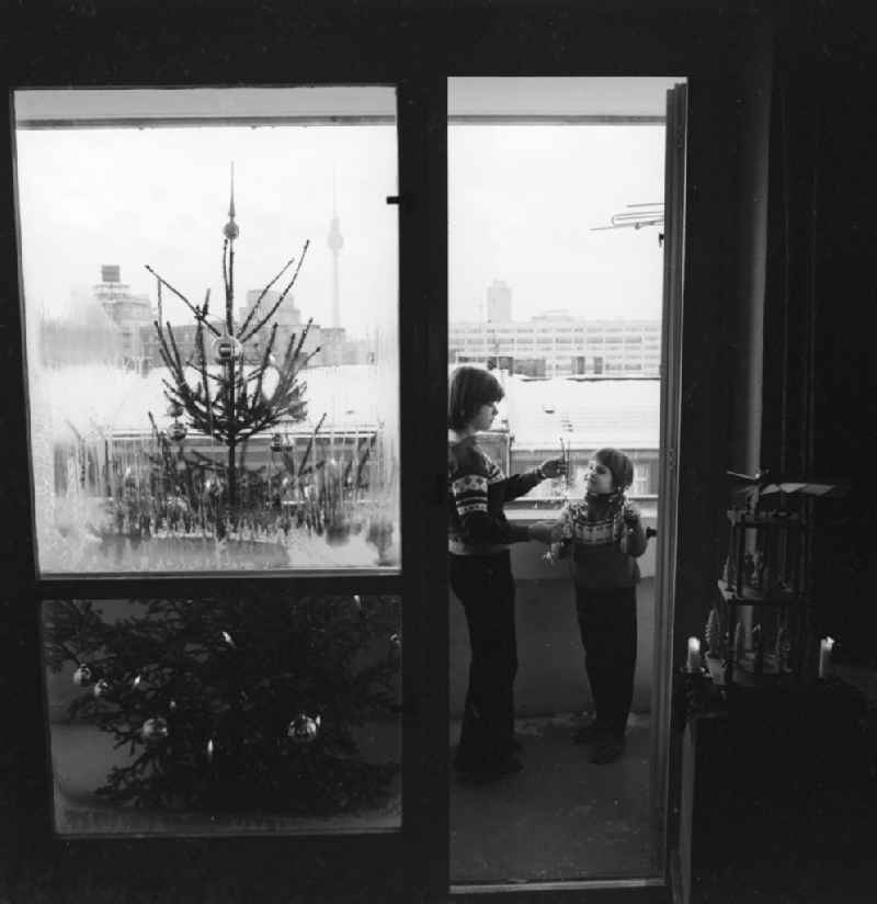 Two children stand with sparklers on a balcony in Berlin. In addition, a decorated Christmas tree