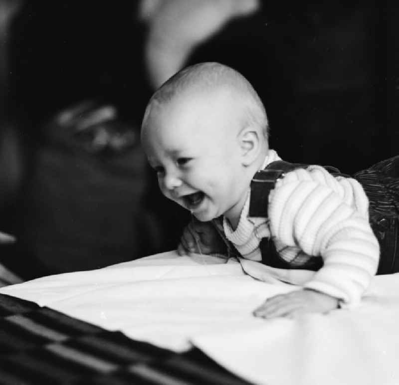 Laughing toddler with overalls on a playmat in Berlin, the former capital of the GDR, the German Democratic Republic