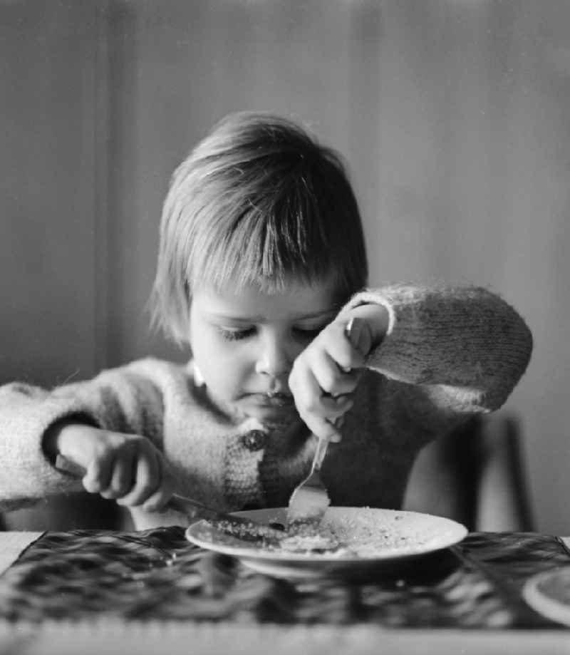 A child eats at the table with knife and fork in Berlin, the former capital of the GDR, the German Democratic Republic