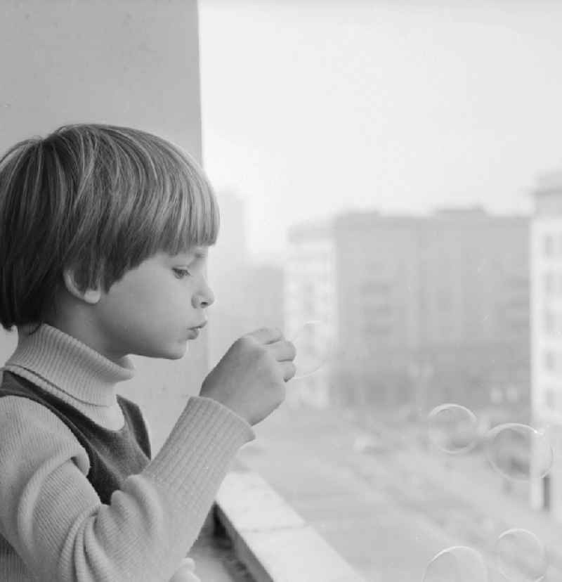 Boy making soap bubbles on a balcony in Berlin, the former capital of the GDR, the German Democratic Republic