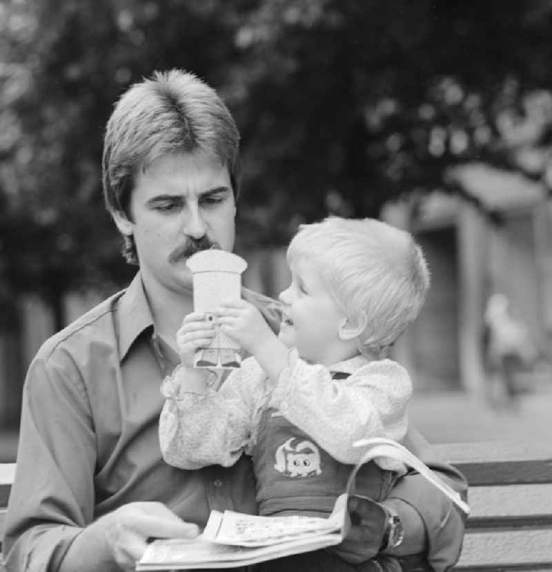 Father sitting with his child on a bench and read a magazine in Berlin, the former capital of the GDR, the German Democratic Republic