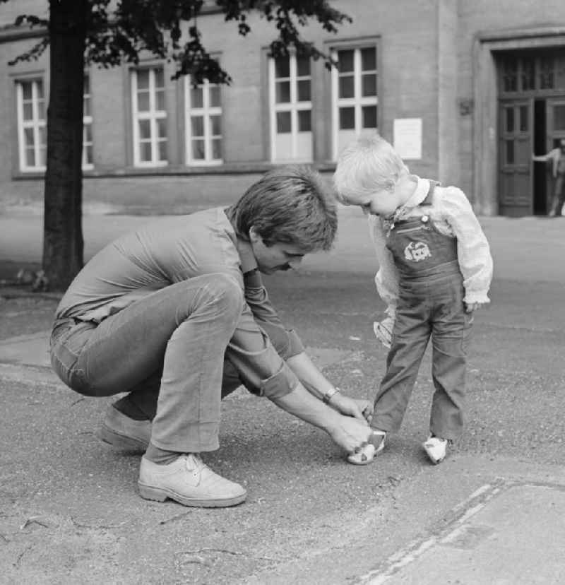 A father binds his child's shoes, in Berlin, the former capital of the GDR, the German Democratic Republic