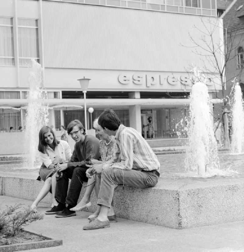 Tourists sitting in front of the Hotel 'Unter den Linden' / Lindencorso the fountain in Berlin, the former capital of the GDR, the German Democratic Republic