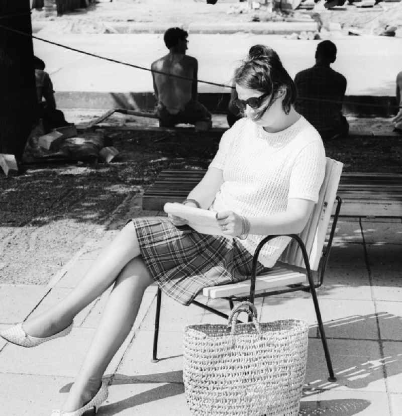 A young woman with sunglasses sitting on a chair and reading a book in Berlin, the former capital of the GDR, the German Democratic Republic