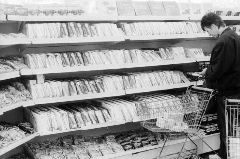 A young woman stands in front of the candy shelf in a department store in Berlin, the former capital of the GDR, the German Democratic Republic. The shelves are filled partly with Ostprodukten as well with Western products