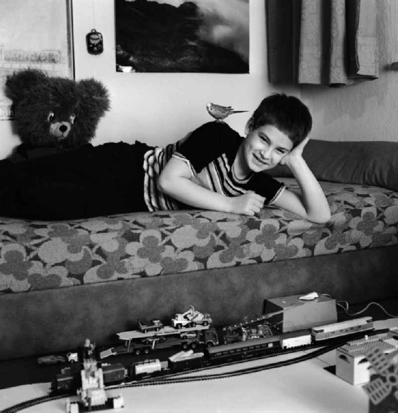 A boy playing with his model railway in his nursery in Berlin, the former capital of the GDR, the German Democratic Republic. His pet, a budgie, sitting on his back and looks on