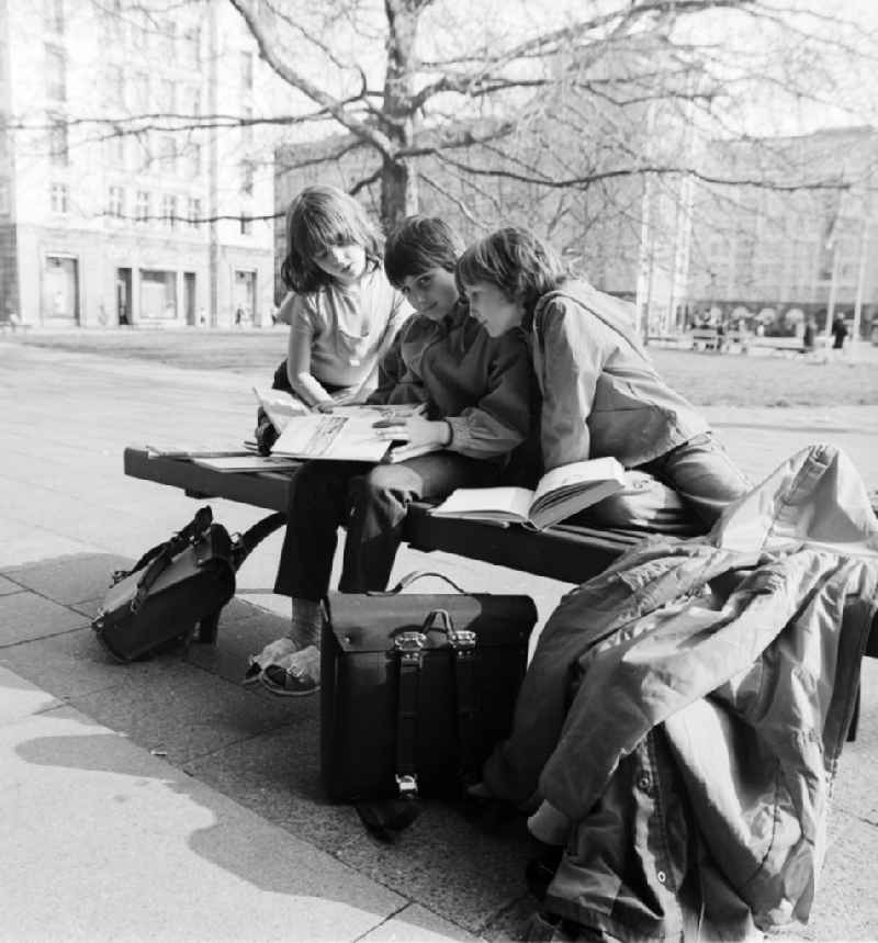 Three children sitting after school on a park bench and reading books, in Berlin, the former capital of the GDR, the German Democratic Republic