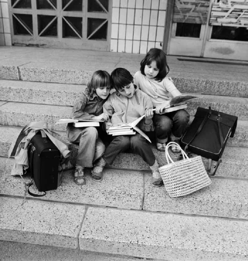 Three children sitting after school in front of a doorway and read books, in Berlin, the former capital of the GDR, the German Democratic Republic