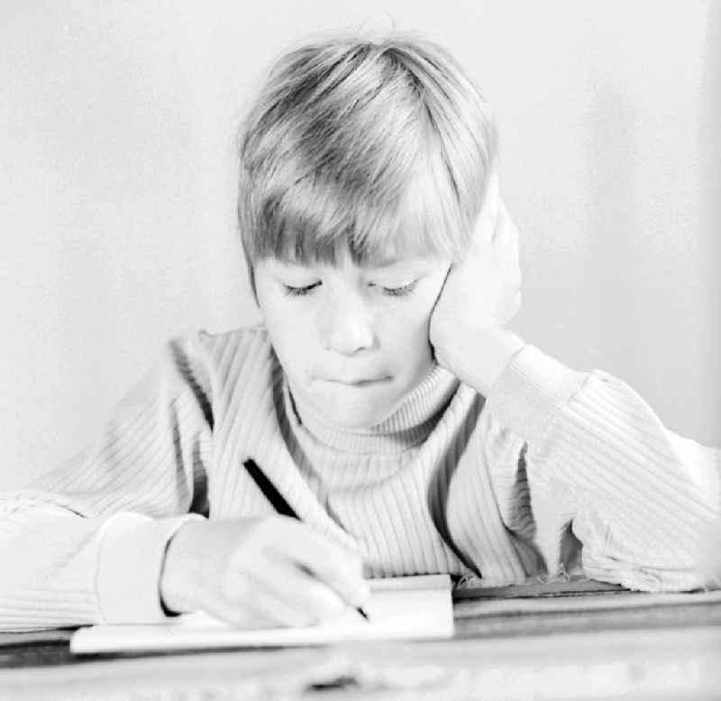 A boy writes with a pen on a piece of paper in Berlin, the former capital of the GDR, German Democratic Republic
