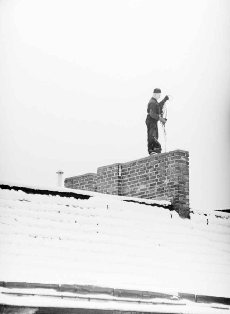 A chimney sweep on snow-covered roofs round the chimneys in Berlin, the former capital of the GDR, German Democratic Republic