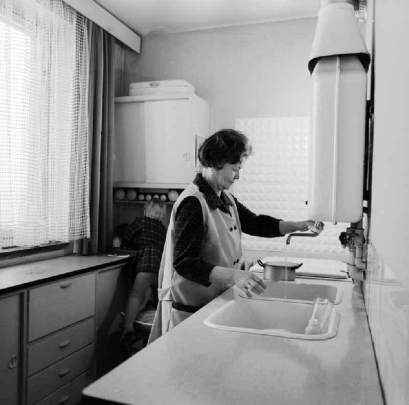 Woman with smock at the wash in the kitchen in Berlin, the former capital of the GDR, German Democratic Republic