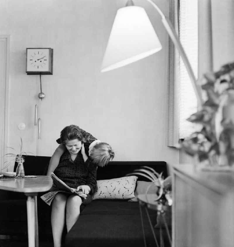 A woman sitting on the sofa in the living room and reading a newspaper, in Berlin, the former capital of the GDR, German Democratic Republic