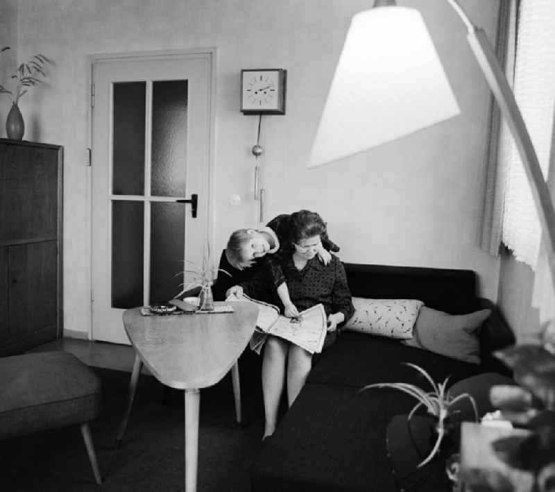 A woman sitting on the sofa in the living room and reading a newspaper, in Berlin, the former capital of the GDR, German Democratic Republic