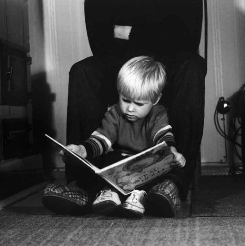 A small child is sitting between the feet of an adult and looks the children's book 'Mother Holle' on, in Berlin, the former capital of the GDR, German Democratic Republic